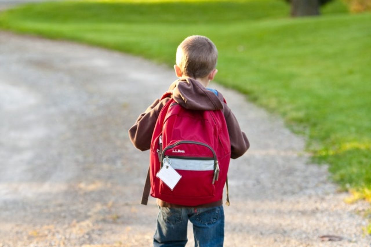 garçon en marron à capuche portant un sac à dos rouge en marchant sur un chemin de terre près de grands arbres 207697 /